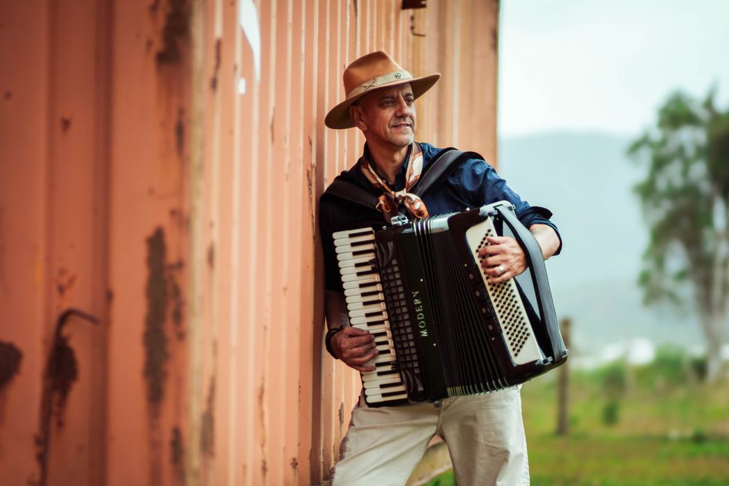 Carlos Magrão tocando gaita encostado numa parede de madeira
